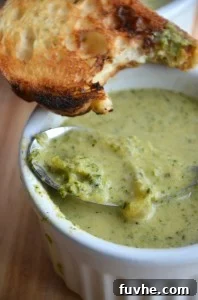 A piece of bread being dipped into a small bowl of creamy vegan cheesy broccoli soup.
