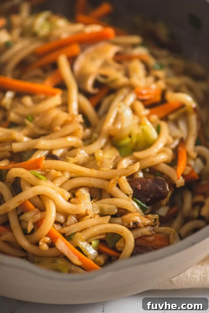 Flavorful Vegan Udon Noodle Stir Fry 5 Close up of a vegan udon noodle stir fry recipe with vegetables being cooked in a large wok.