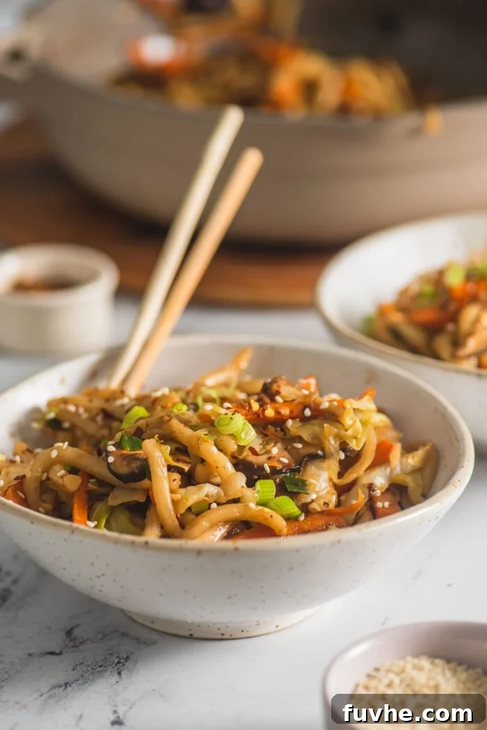 Flavorful Vegan Udon Noodle Stir Fry 6 Set of chopsticks resting in a small bowl of vegetable udon noodle stir fry, ready to be eaten.