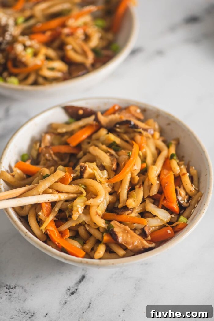 Flavorful Vegan Udon Noodle Stir Fry 7 Two chopsticks resting in a bowl of yaki udon noodle stir fry with cabbage, carrot and mushroom, ready to be eaten.