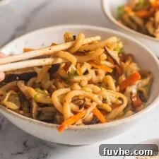Hand using a set of chopsticks in a bowl of yaki udon.