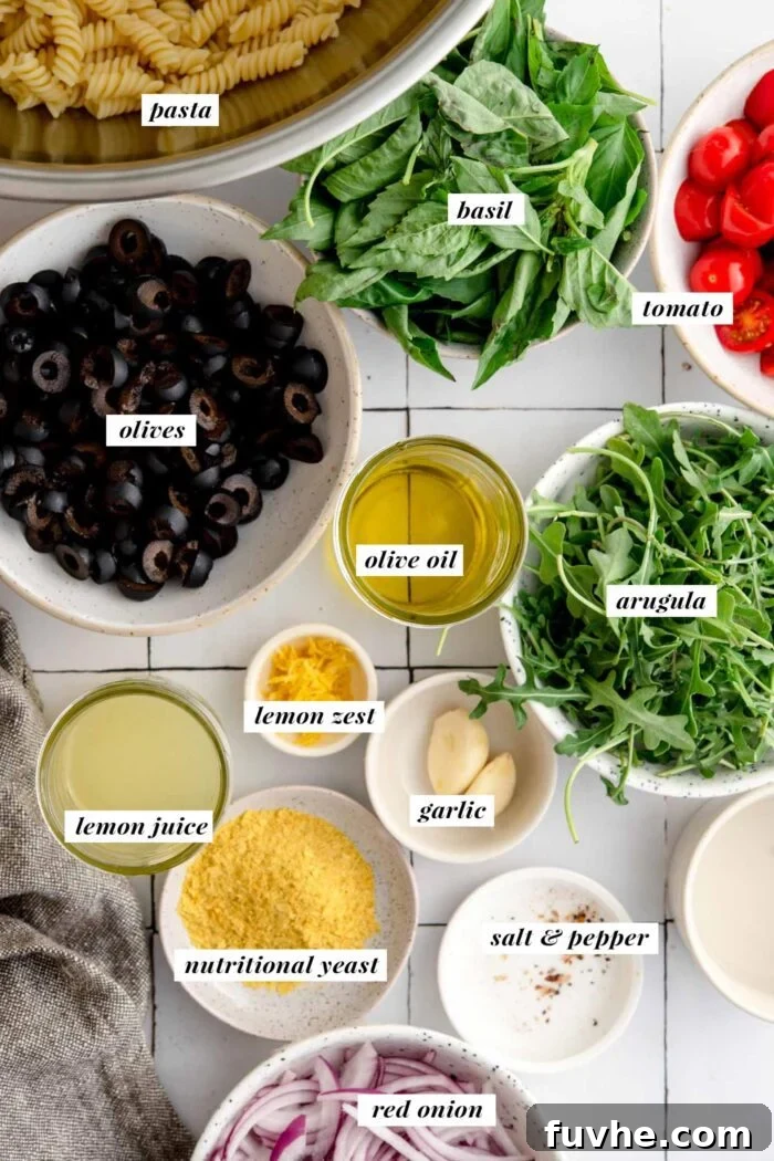 Vibrant Vegan Pesto Pasta Salad 3 An overhead view showcasing the fresh, vibrant ingredients essential for crafting a cold pesto pasta salad recipe, including plump olives, thinly sliced red onion, aromatic basil leaves, crisp arugula, and juicy tomatoes.