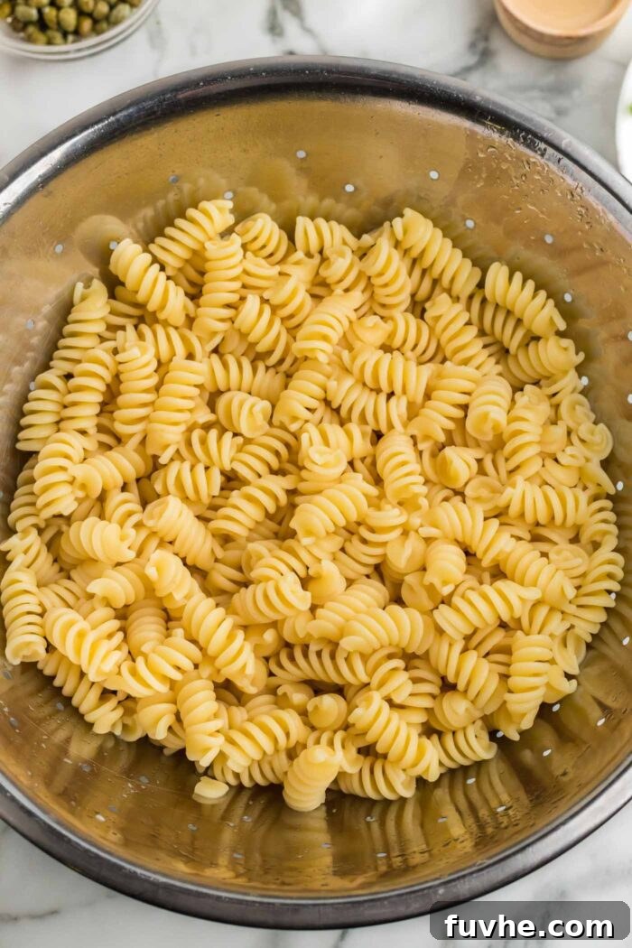 Vibrant Vegan Pesto Pasta Salad 4 Freshly cooked rotini pasta noodles, perfectly al dente, resting in a gleaming metal colander after being rinsed. This image captures an essential step in preparing a cold pasta salad, ensuring the noodles are ready to absorb the flavorful pesto.