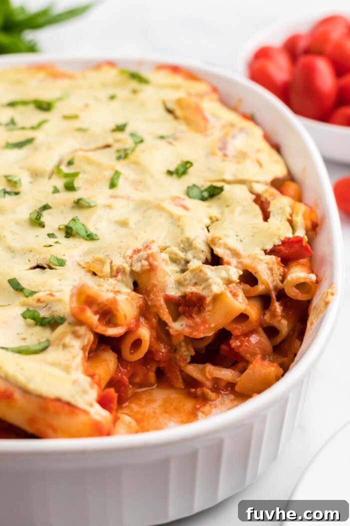 Hearty Plant-Based Baked Ziti 11 Baked ziti topped with ricotta cheese in a white oval baking dish. A small dish of tomatoes is in the background.