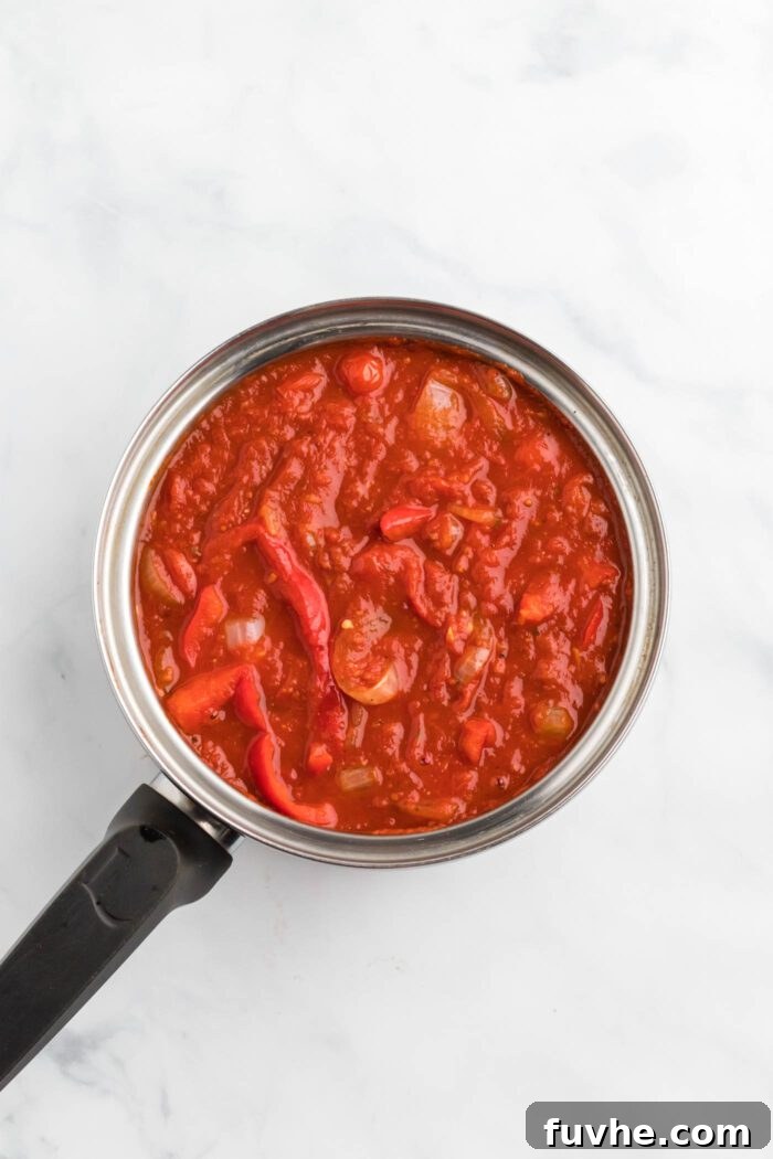 Hearty Plant-Based Baked Ziti 6 Red tomato sauce with onion and bell pepper cooking in a saucepan.