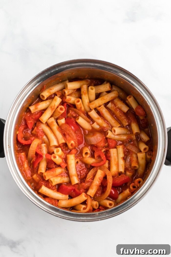 Hearty Plant-Based Baked Ziti 8 Ziti pasta mixed with tomato sauce, onion, and bell pepper in a saucepan.