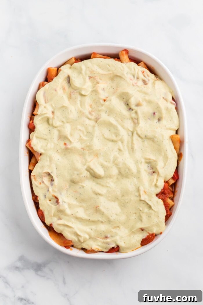 Hearty Plant-Based Baked Ziti 9 Ziti in tomato-based pasta sauce topped with a layer of tofu ricotta in an oval baking dish.
