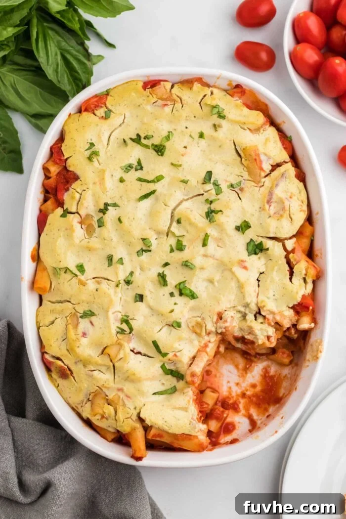 Hearty Plant-Based Baked Ziti 10 Overhead view of vegan baked ziti topped with fresh chopped basil with a scoop taken out of it in an oval baking dish.