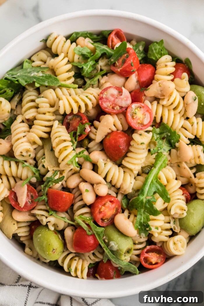 An inviting overhead shot of a finished zesty Italian pasta salad, brimming with colorful rotini pasta, fresh greens, halved cherry tomatoes, tender artichoke hearts, and fragrant fresh herbs, all coated in a vibrant dressing. It looks ready to be served and enjoyed.