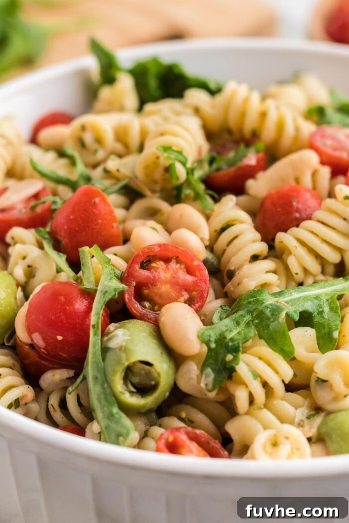 A close-up, mouth-watering shot of a zesty Italian pasta salad, highlighting the vibrant interplay of halved cherry tomatoes, briny olives, fresh arugula, and colorful pasta spirals, all generously coated in a bright, savory Italian dressing.