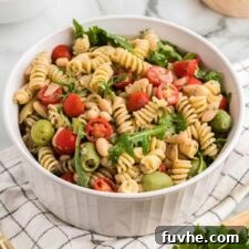 Large bowl of zesty Italian pasta salad with artichokes, olives, tomato and arugula.