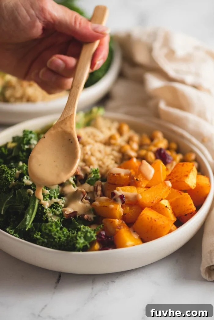 Vibrant Vegan Quinoa Fuel Bowls 8 A hand using a spoon to gracefully drizzle creamy dressing over a beautifully assembled healthy bowl of kale, quinoa, and roasted squash.