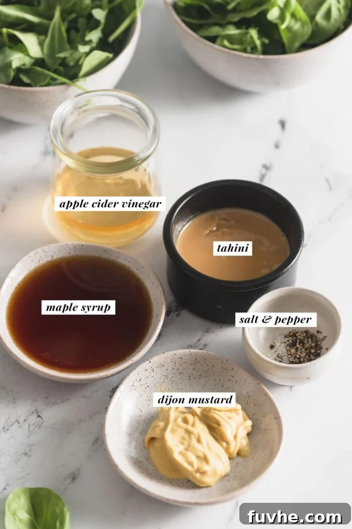 Dijon mustard, maple syrup, tahini, apple cider vinegar and salt and pepper in small bowls. Each ingredient is labelled with text.