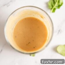 Overhead view into a jar of creamy tahini dijon maple dressing with a few pieces of spinach around it.
