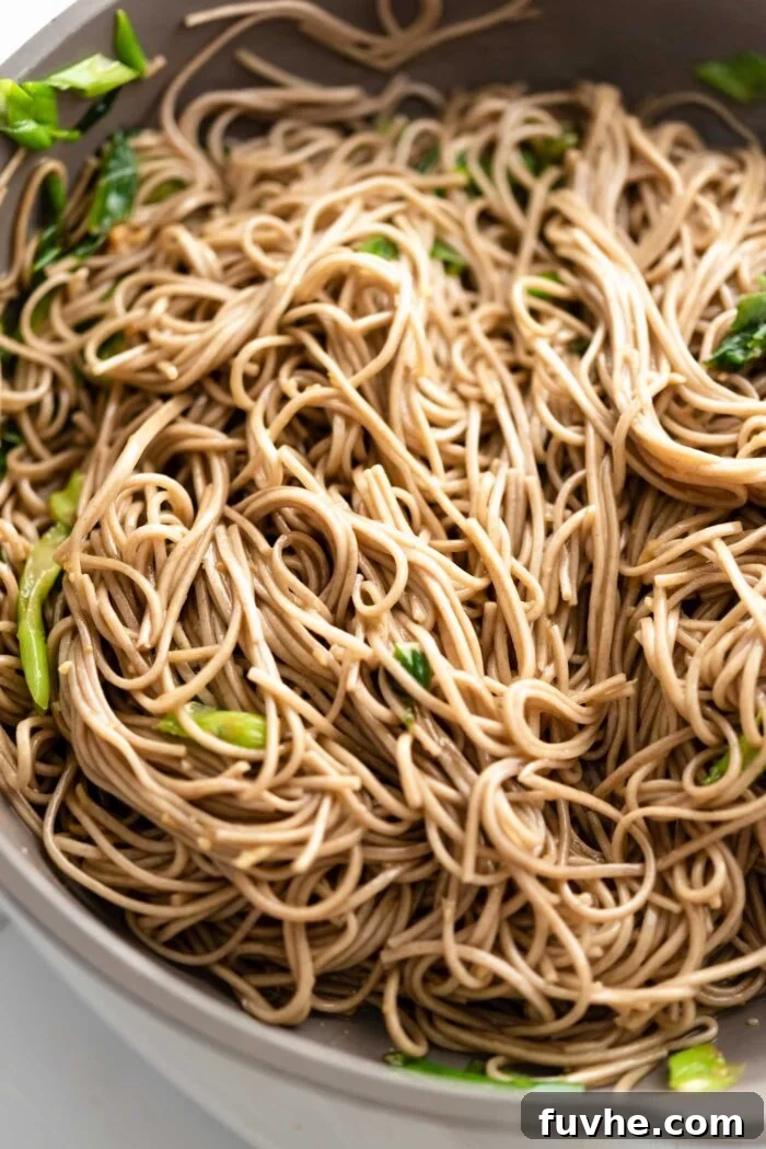 Zesty Soba Noodle Delight 6 Soba noodles in sesame garlic sauce with green onions cooking in a pan.