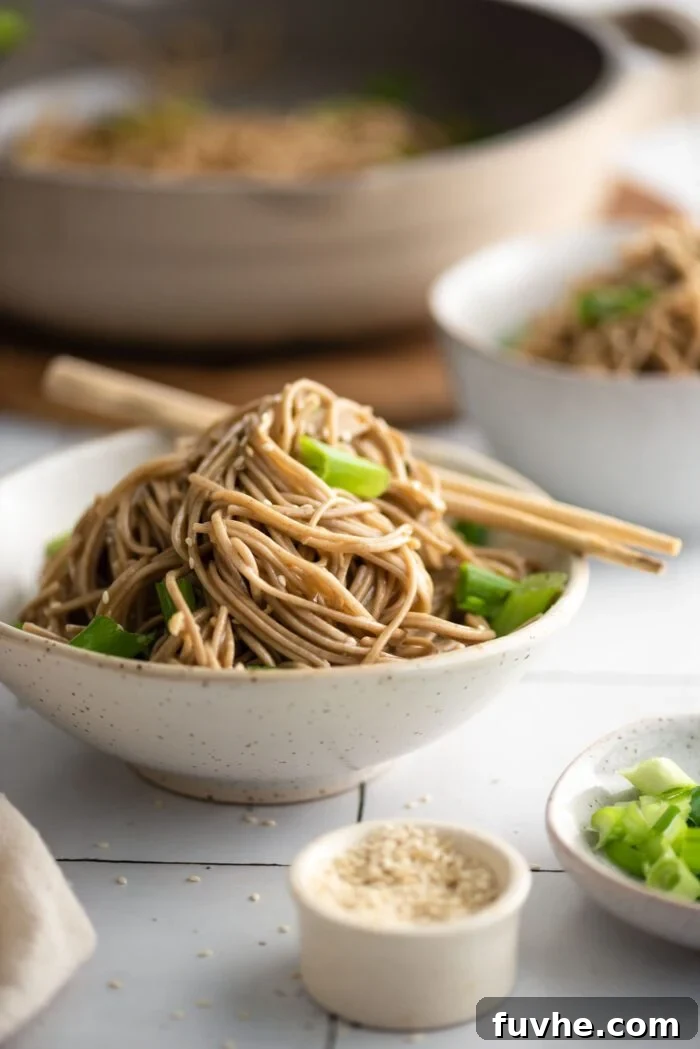 Zesty Soba Noodle Delight 7 Bowl of sesame buckwheat soba noodle salad with green onions, topped with sesame seeds. A pair of chopsticks rests on the side of the bowl.