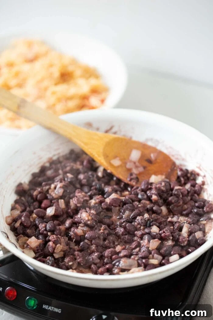 Hearty Vegan Black Bean Burritos 5 Black beans with diced onions and spices cooking in a skillet on a cooktop, ready to be mashed and infused with flavor.