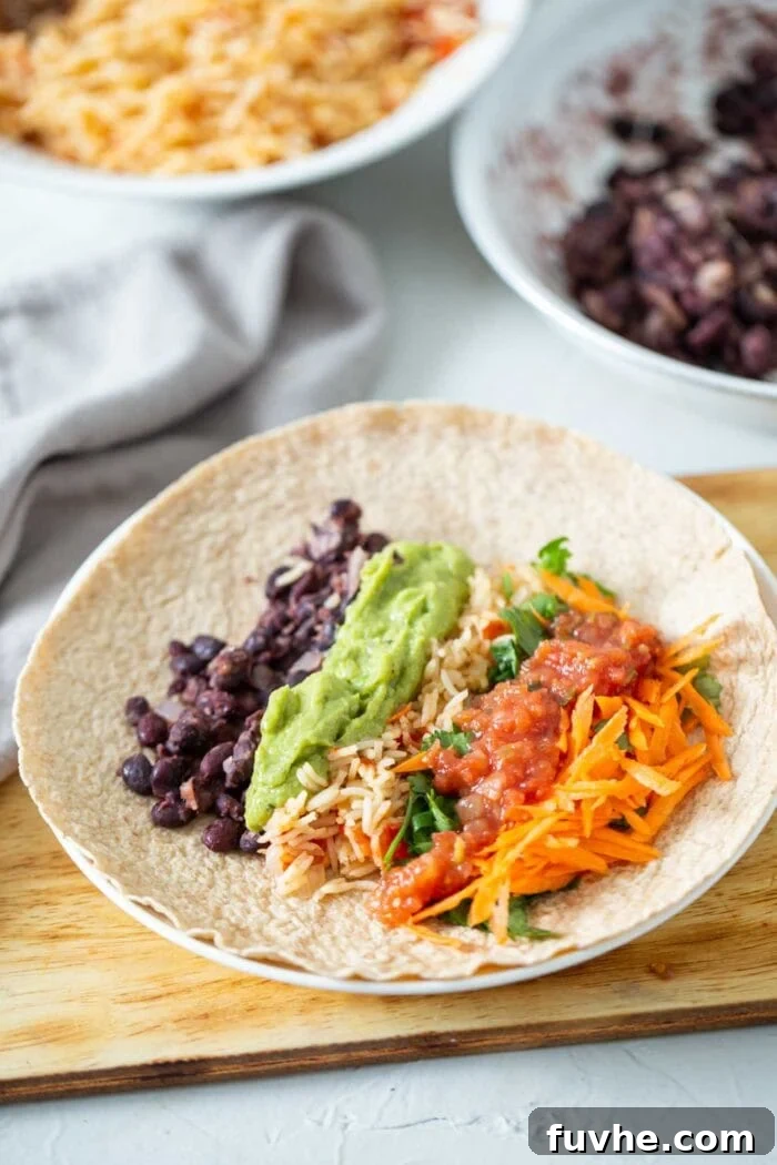Hearty Vegan Black Bean Burritos 6 A large tortilla laid flat, generously filled with avocado, tomato rice, spiced black beans, and shredded vegetables, ready for rolling.