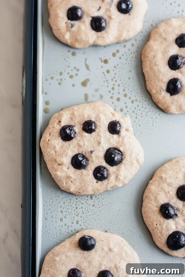 Vegan coconut pancakes with blueberries gently sizzling on a hot pancake griddle, turning golden brown.