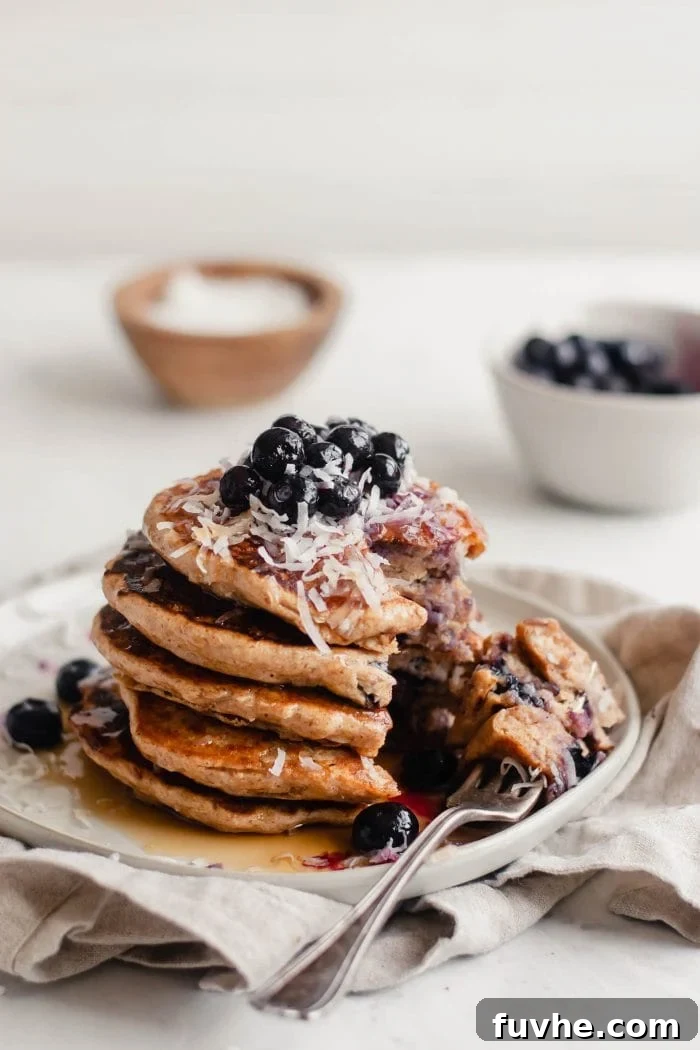 A stack of vegan blueberry coconut pancakes, beautifully garnished with a scattering of fresh blueberries and shredded coconut on top.