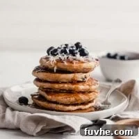 Stack of vegan blueberry coconut pancake with blueberries and coconut on top.