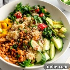 A colourful quinoa grain bowl with avocado, mango, tempeh, cucumber, cilantro, tomato, kale and green onion.