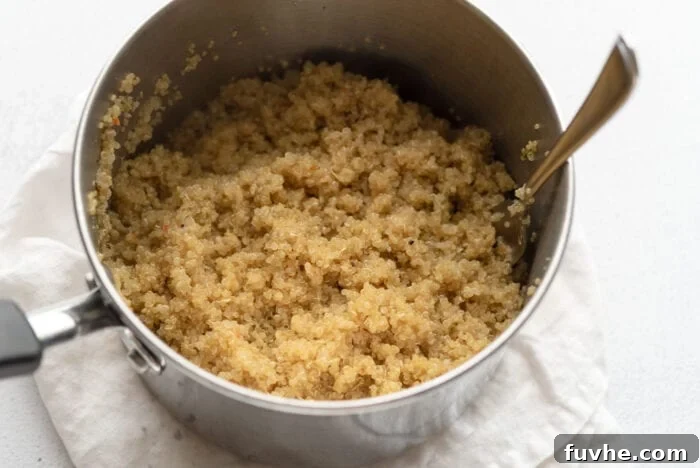 A pot of fluffy cooked quinoa with a fork resting in it. The pot is sitting on a folded dish cloth.