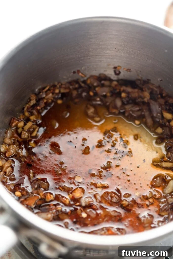 Hot chili maple sauce with shallot, ginger and garlic cooking in small saucepan.