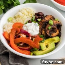 Easy veggie fajita bowls with cooked bell peppers and onions, avocado, rice, sour cream, black beans and marinated cooked mushrooms.