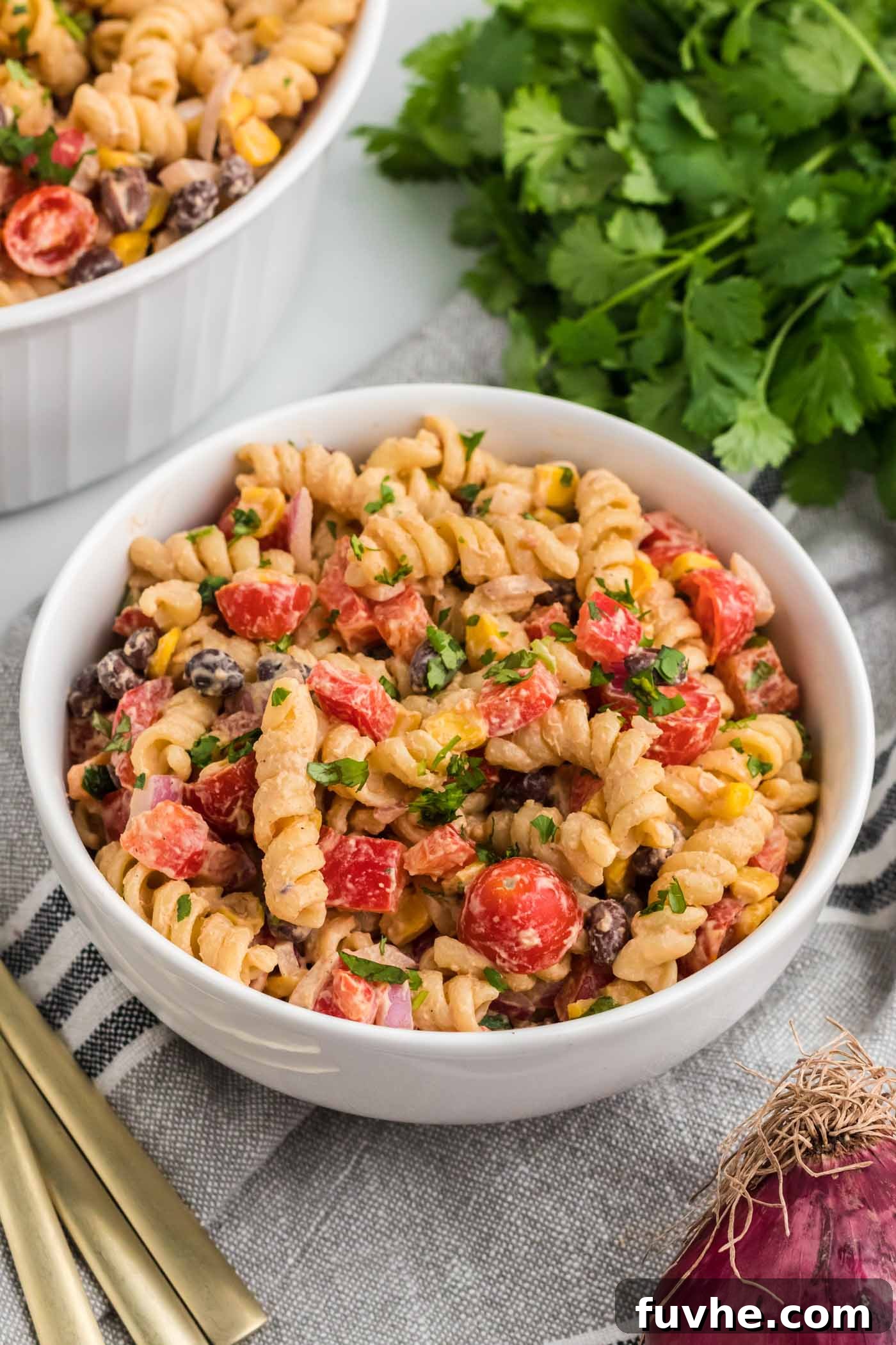 Chipotle Lime Vegan Pasta Salad 2 A bowl of creamy vegan Southwestern pasta salad with black beans, peppers and corn. There's cilantro in the background and a larger serving bowl of the salad.