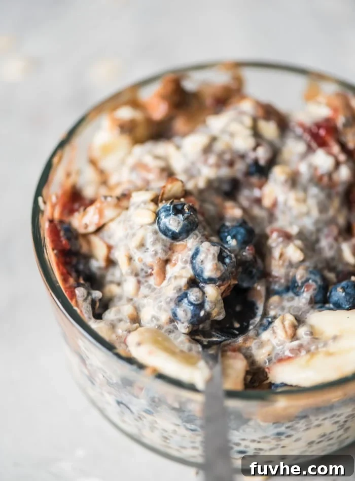 Overnight Banana Bliss 3 A close-up view of a wholesome bowl of overnight chia seed oats, beautifully adorned with crunchy almonds, fresh blueberries, a dollop of sweet jam, and delicate slices of banana. A spoon rests invitingly in the bowl, ready to be enjoyed.