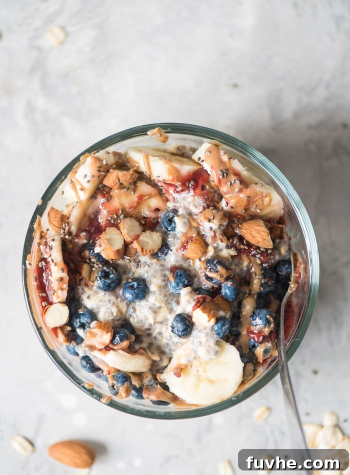 Overnight Banana Bliss 4 An inviting overhead shot of a bowl of overnight chia seed oats, beautifully garnished with crisp almonds, juicy blueberries, a swirl of jam, and fresh banana slices. A spoon is gently placed in the bowl, inviting a taste.