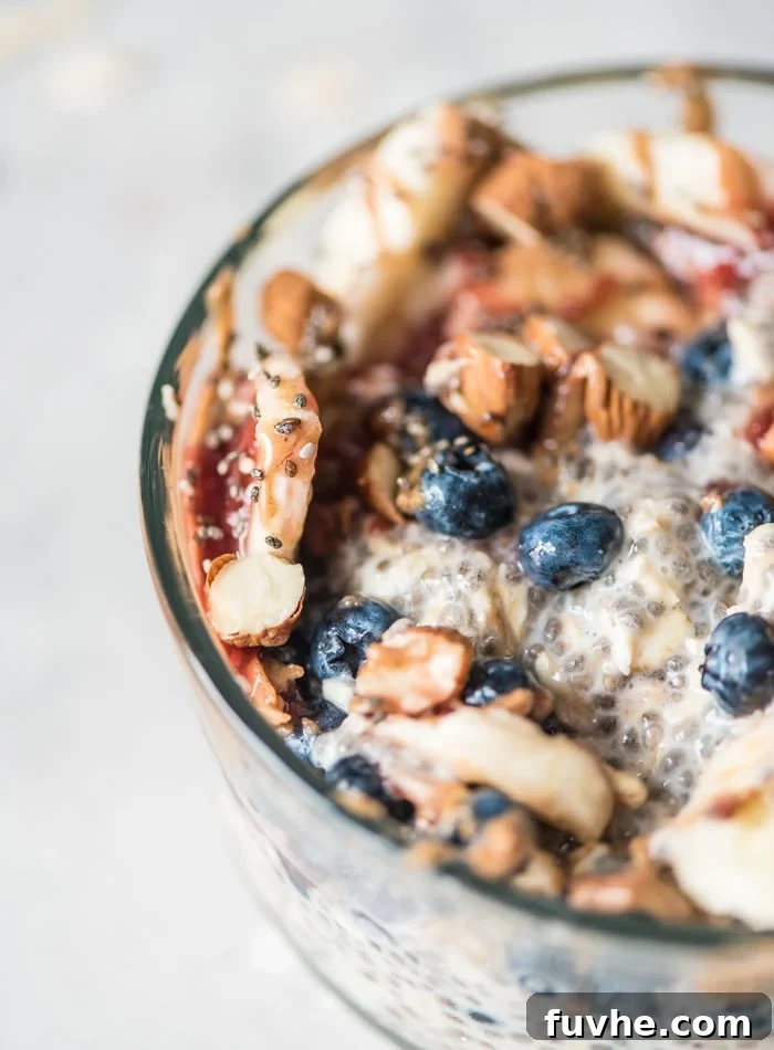 Overnight Banana Bliss 5 A sumptuous close-up of a bowl of overnight chia seed pudding with oats, luxuriously topped with slivered almonds, plump blueberries, a spoonful of rich jam, and perfectly ripe banana slices. This enticing view highlights the creamy texture and fresh additions.