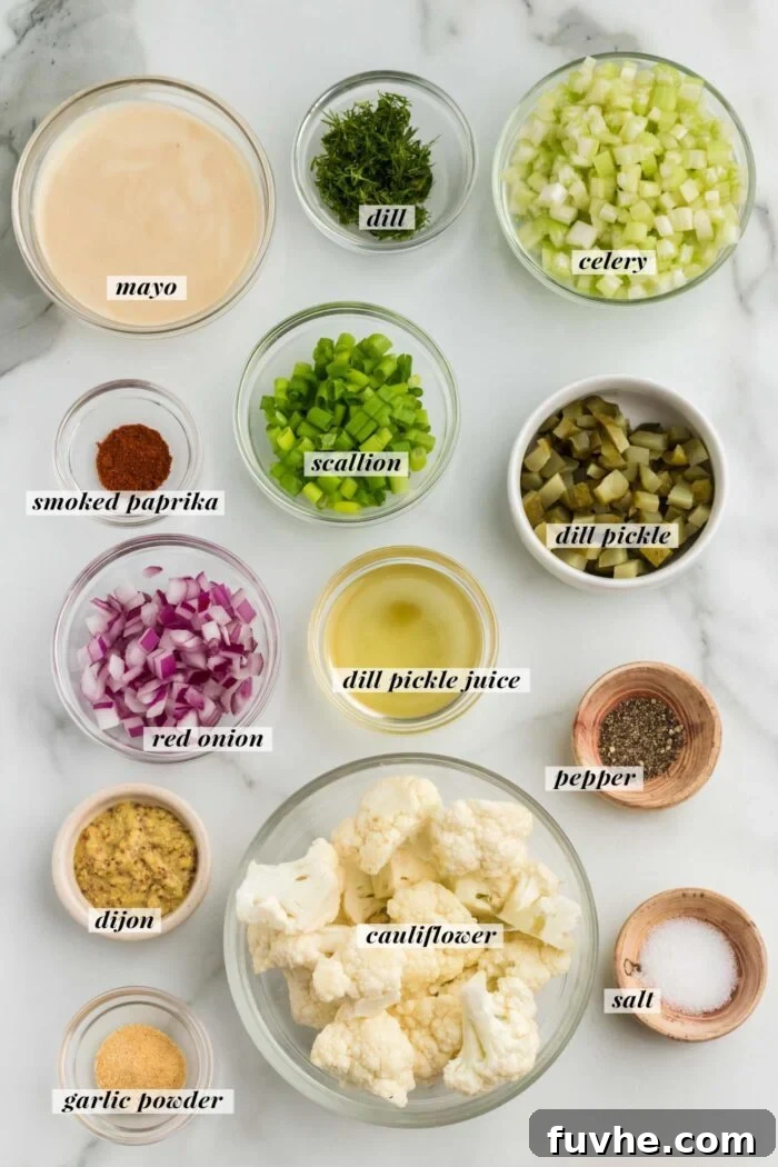 A beautifully arranged flat lay displays all the fresh ingredients for making a cauliflower "potato" salad. Bowls contain crisp dill pickles, thinly sliced red onion, crunchy celery, and aromatic spices, each ready to contribute to the salad\