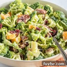 Broccoli apple salad with cranberries, pecans and brussels sprouts in a salad bowl with a spoon.