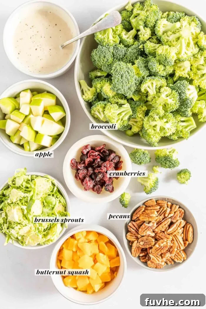 Bowls filled with individual ingredients for broccoli apple salad: diced apple, fresh broccoli florets, chopped pecans, roasted butternut squash cubes, shredded Brussels sprouts, and dried cranberries.
