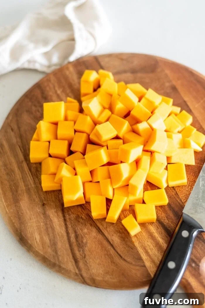 Three cups of perfectly peeled and cubed butternut squash resting on a cutting board, alongside a sharp knife, ready for cooking.