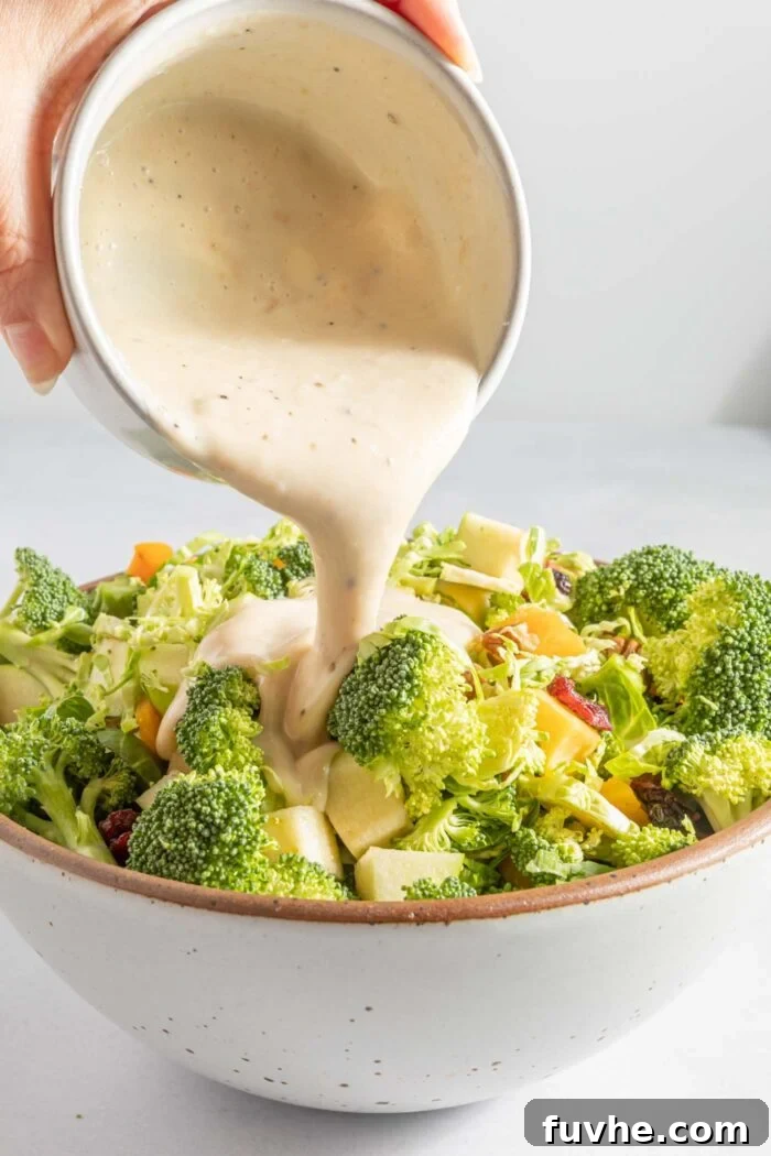 The creamy mayonnaise dressing being artfully poured over a colorful broccoli apple salad, nestled in a large salad bowl, ready for a final toss.