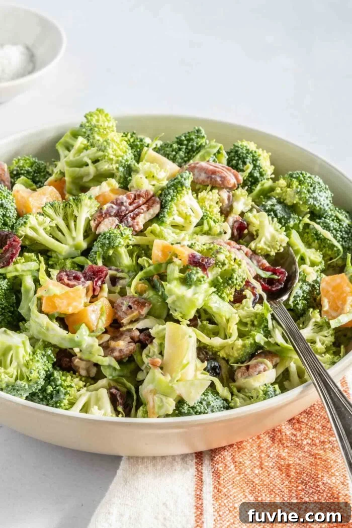 A vibrant bowl of creamy broccoli apple salad, adorned with bright cranberries, crunchy pecans, and thinly sliced Brussels sprouts, ready to be enjoyed with a spoon.