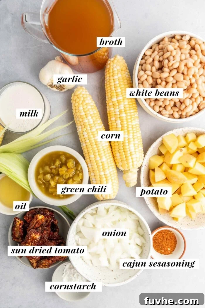 Sunny Vegan Corn Chowder 3 A vibrant assortment of fresh ingredients neatly arranged on a countertop, including several ears of corn, diced potatoes, onions, garlic cloves, sun-dried tomatoes, canned white beans, and a can of green chilies, all prepped for making a delicious corn chowder.