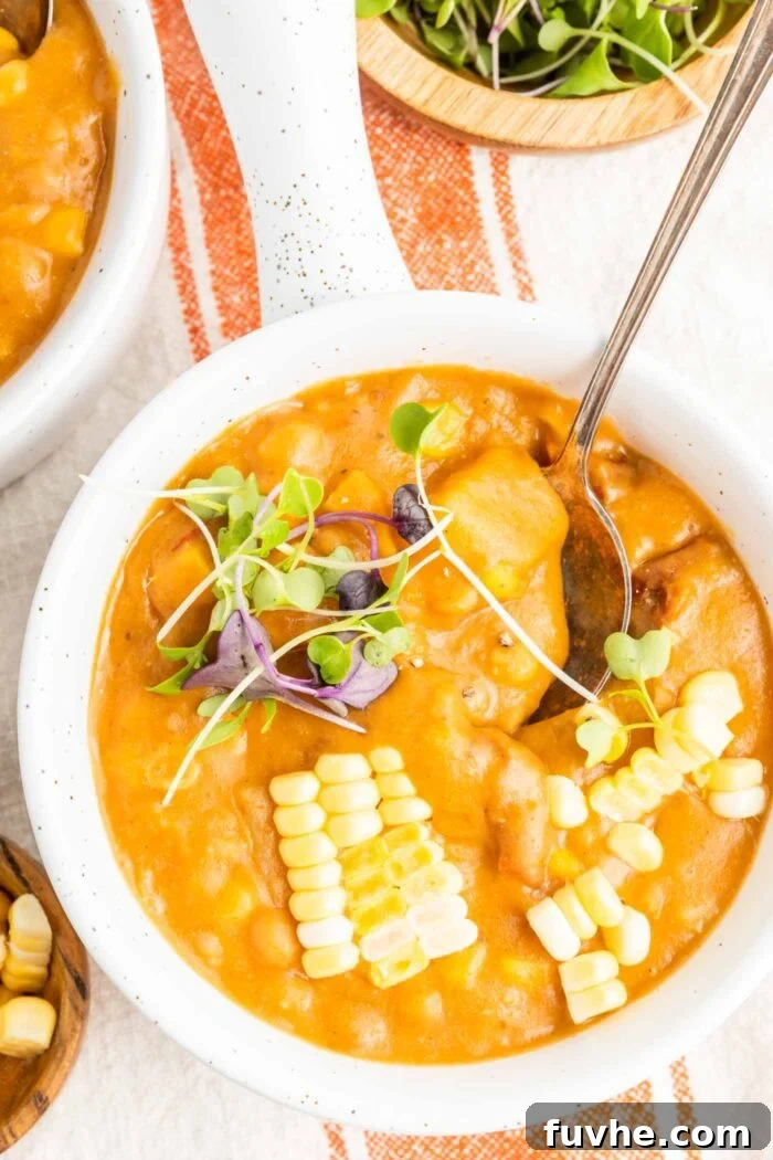 Sunny Vegan Corn Chowder 8 Close-up overhead view of a beautifully garnished bowl of summer corn chowder, rich with sun-dried tomatoes and tender potatoes. It's elegantly topped with vibrant corn kernels and delicate microgreens, inviting a delicious first bite.
