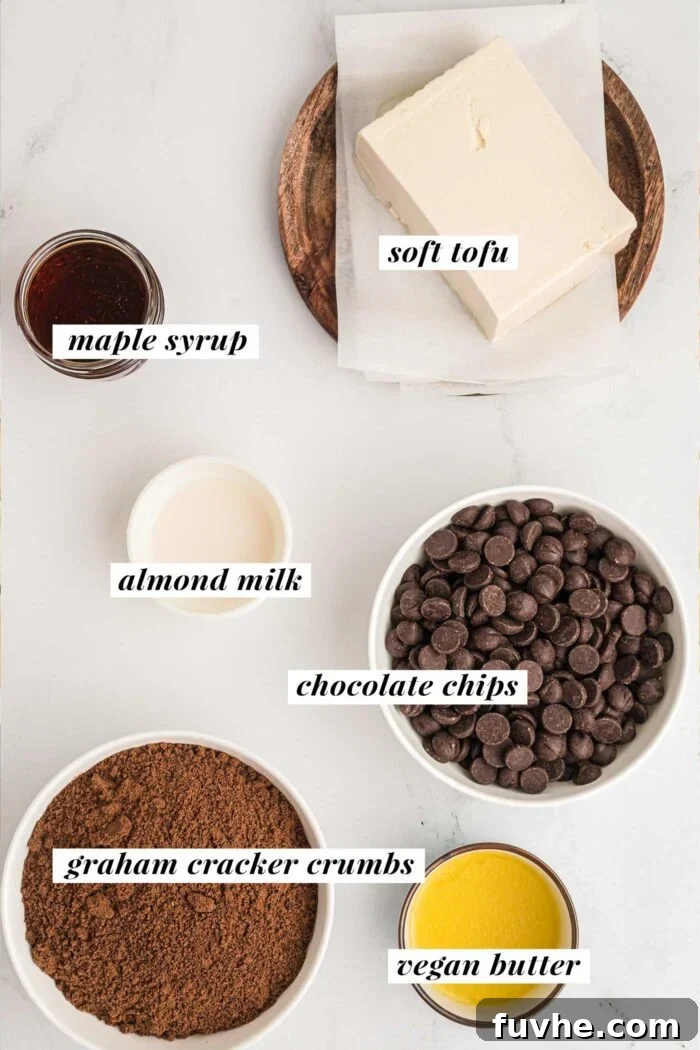 Small bowls containing the essential ingredients for the vegan chocolate pie: chocolate chips, soft tofu, plant-based milk, maple syrup, graham cracker crumbs, and melted plant-based butter. Each bowl is clearly labeled.