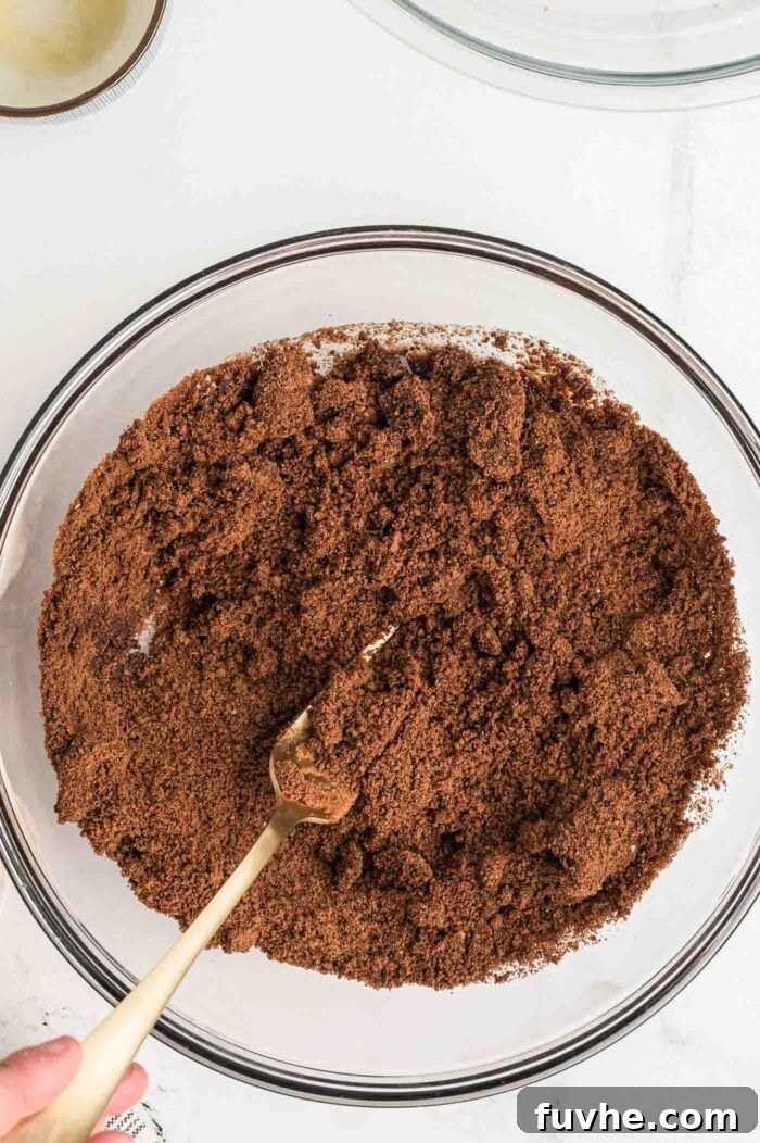 Mixing crushed chocolate graham crackers and melted plant-based butter together in a bowl with a fork, creating the base for the pie crust.