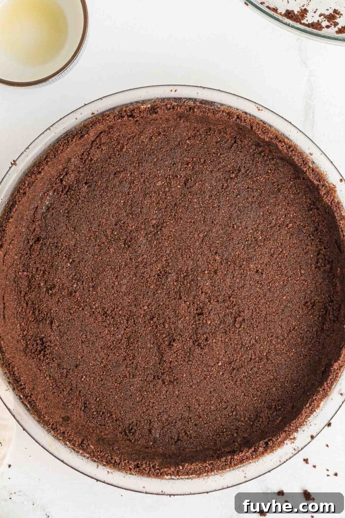 A chocolate graham cracker pie crust firmly pressed into a round 9-inch glass pie dish, ready for chilling.