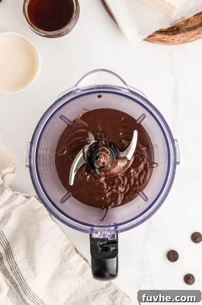 Smooth, melted vegan chocolate in a food processor container, with a few chocolate chips scattered nearby.