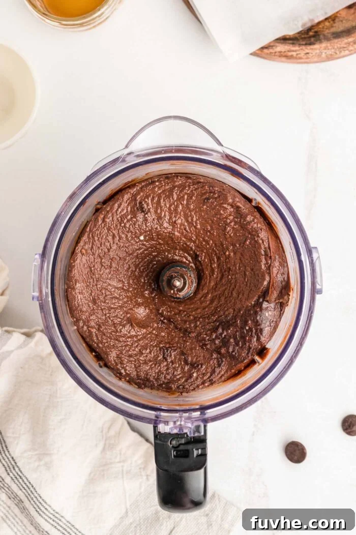 A creamy, luscious chocolate pie filling mixture swirling in a food processor container, indicating a perfectly blended consistency.