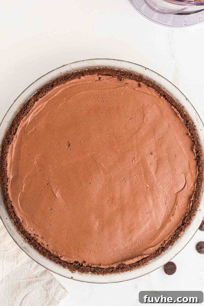 An overhead view of a no-bake vegan chocolate pie with its chocolate crust in a glass pie dish, after the filling has been added and smoothed.
