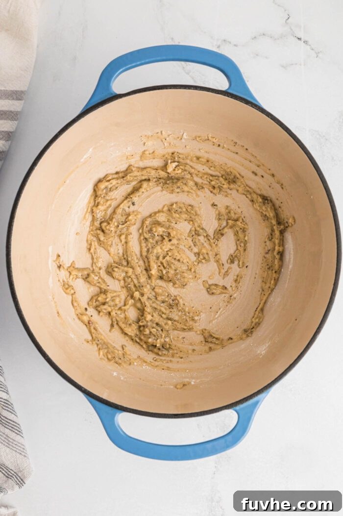 Flour and dried herbs mixed with melted plant-based butter in a large pot, forming the base of a creamy roux for the pot pie filling.