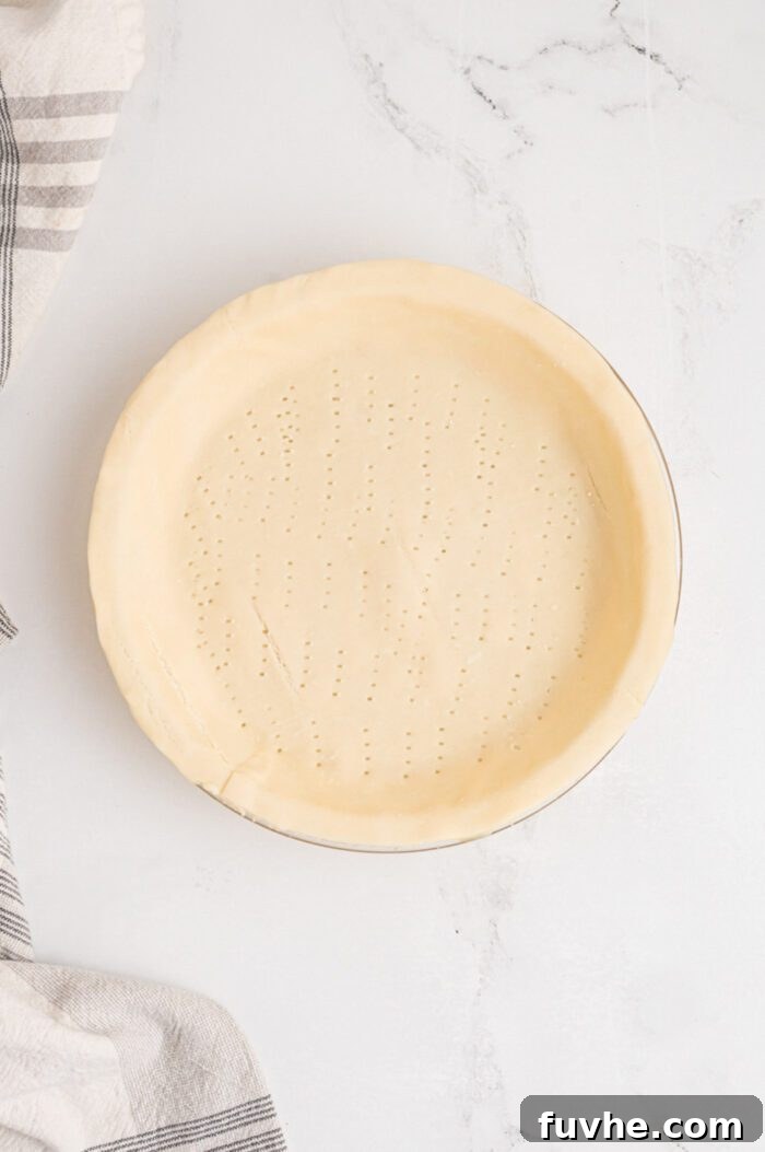 An unbaked pie crust expertly pressed into a 9-inch pie dish, with small, evenly spaced perforations created by a fork on the bottom of the crust.