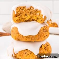 Stack of 3 soft pumpkin cookies topped with icing. The cookie on top has a bite out of it so you can see the texture inside.